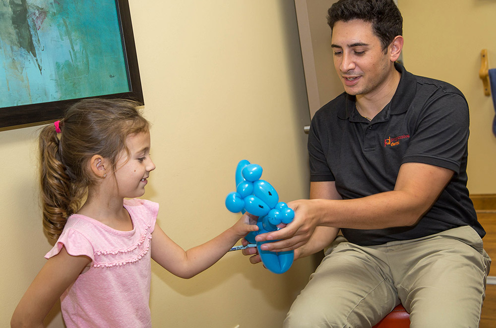 Dr. Marcus Spera giving a little girl a balloon animal after her visit