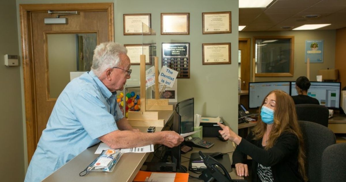 A male patient standing at the front desk, smiling as he hands a check to the receptionist after his dental appointment